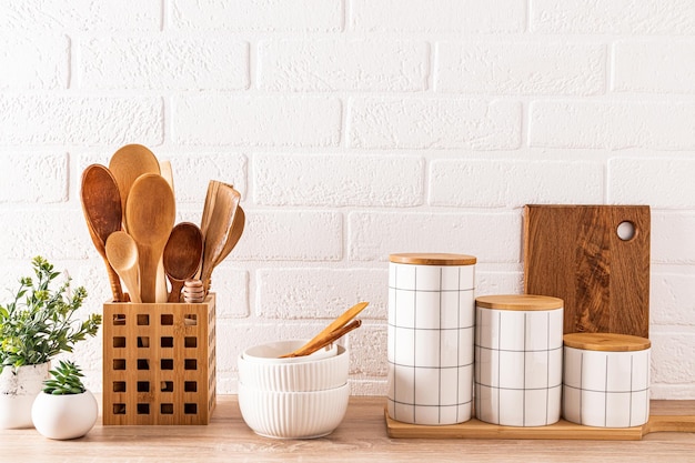 Set of stylish ceramic food storage jars ceramic bowls wooden spoons in a stand on a wooden countertop with potted indoor plants