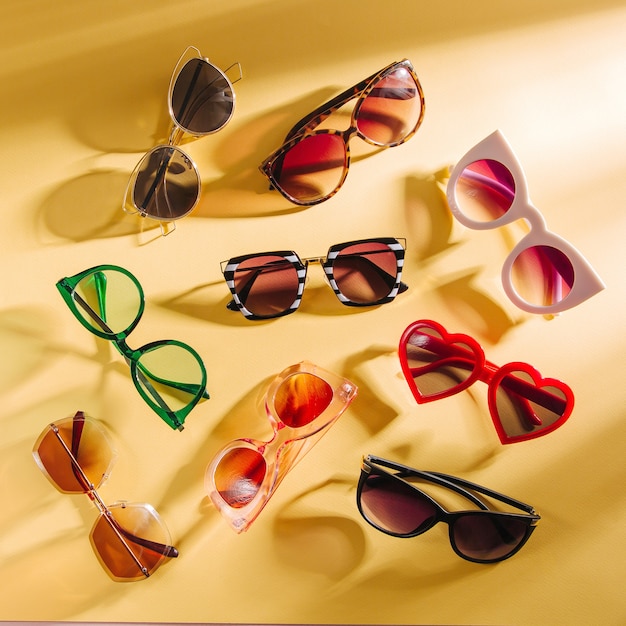 set of stylish sunglasses with bright sunlight on yellow background flat lay top view