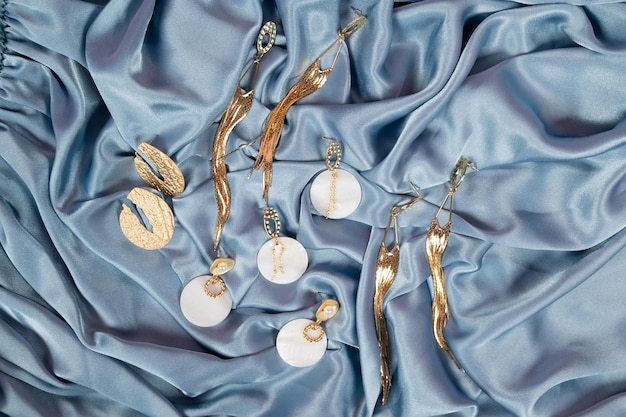 A set of stylish trendy gold earrings on crumpled blue fabric bacground Gold earrings with shell rock and pearls