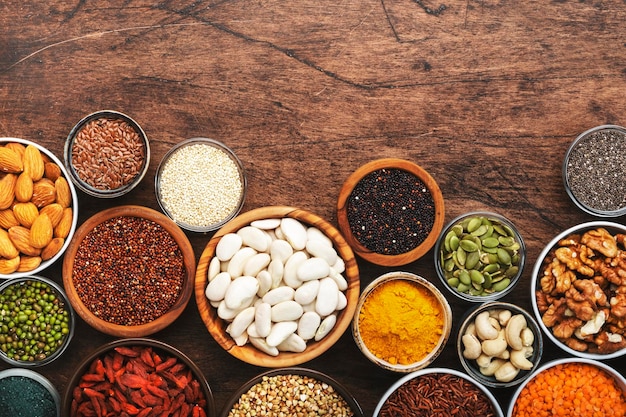 Set of superfoods legumes cereals nuts seeds in bowls on wooden table Copy space top view