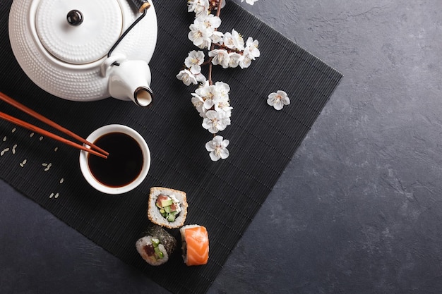 Set sushi en maki broodjes met tak van witte bloemen en theepot met de inscriptie groene thee op stenen tafel. Bovenaanzicht.