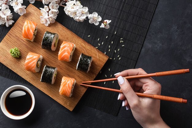 Set sushi, maki broodjes, hand met stokjes en tak van witte bloemen op stenen tafel. Bovenaanzicht.