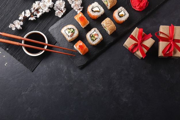 Set of sushi, maki rolls, gift boxes with branch of white flowers on stone table Top view.