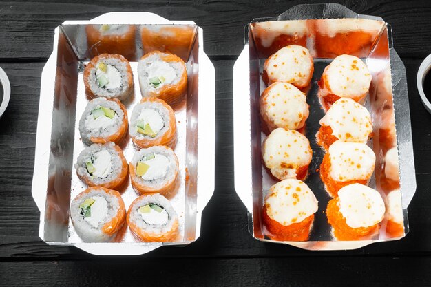 Set di rotoli di sushi in scatola per alimenti per la consegna, su tavolo in legno nero