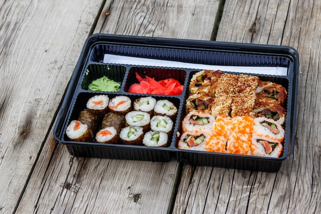 Set of sushi rolls in plastic box on wooden table