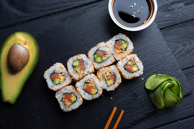 Set of sushi rolls with cream cheese, rice and salmon on a black board decorated with soy sauce and avocado on a dark wooden table. Japanese cuisine. Food photo table