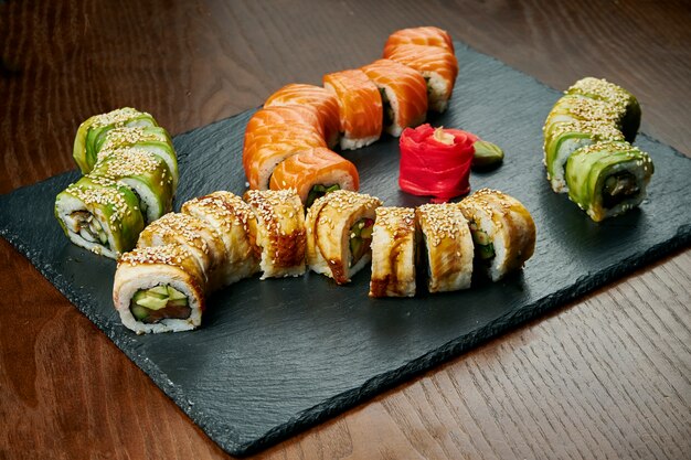 Set di involtini di sushi con cetriolo e salmone, anguilla, avocado e tonno su una tavola di ardesia nera su un tavolo di legno. cucina giapponese.