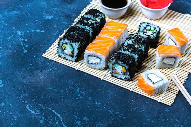 Set of sushi rolls with salmon and with omelet, tofu and vegetables, flying fish roe, tempura on makisu. Traditional Japanese food.