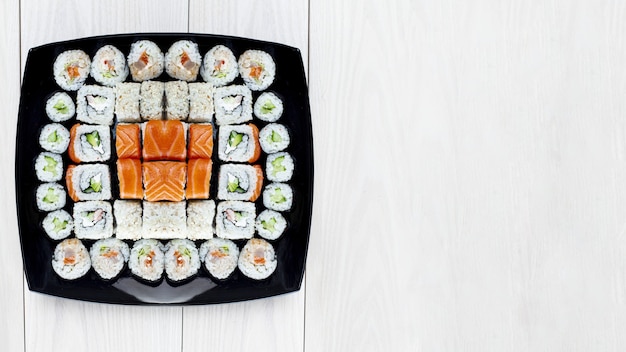 Set sushi rolt uit verschillende niveaus van verschillende rollen op een zwarte plaat. Lichte houten achtergrond. Plaats voor tekst. Zachte focus. Japans sushi-concept.