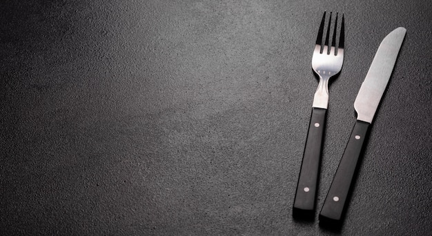 Set of tableware ready for the meal with black copy space. Metal knife, fork, spoon and plate