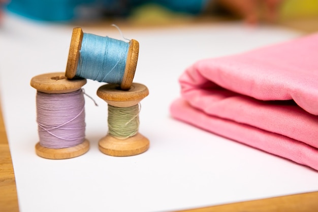 Set of tailoring accessories. Close up of a stack of folded pink fabric, sewing scissors, and spools of thread