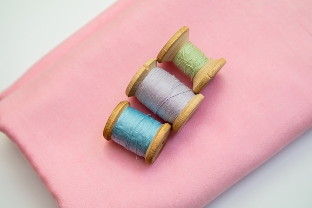 Set of tailoring accessories. Close up of a stack of folded pink fabric, sewing scissors, and spools of thread