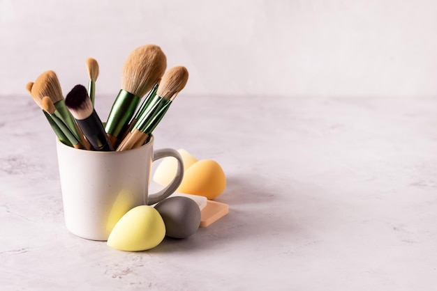 Set of Tassels for Make Up in Cup and Set of Make Up Eggs on Gray Background Horizontal Copy Space