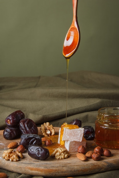 Set for Tea drinking. Hand holding spoon with dripping honey. Various sweets, nuts and honey for tea on a wooden cutting board. Healthy sweets, delicious dessert, natural sweets.