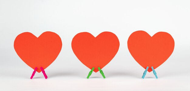 Set of three paper hearts stands on wooden clothespins on white background. Minimal love concept.