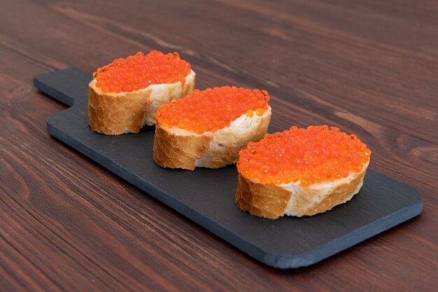 Photo set of three sandwiches with red caviar on the grey stone board