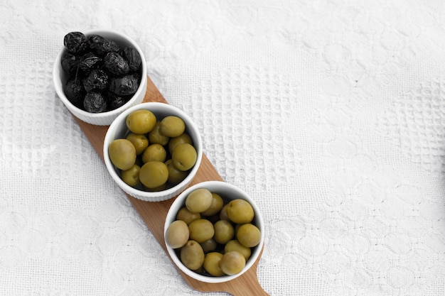 Set of three white bowls with olives on wooden tray on white blanket