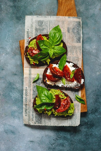 Set of tomato bruschetta with cottage cheese cherry tomatoes avocado guacamole basil lime served on wooden cutting board