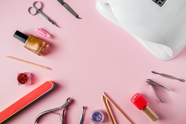 Un set di strumenti per manicure e cura delle unghie su uno sfondo rosa.