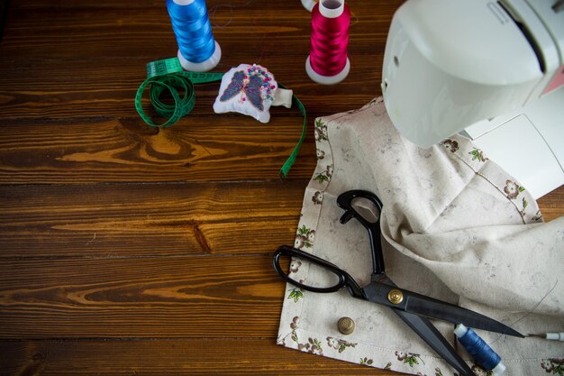 A set of tools and threads for sewing clothes on a wooden background