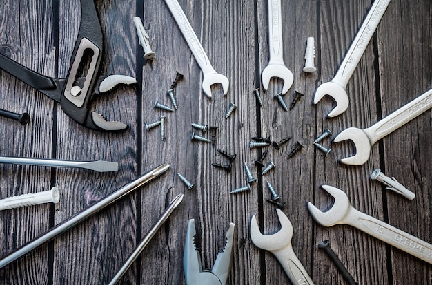 A set of tools on a wooden background: screwdrivers, pliers, adjustable wrench, open-end wrench, screws, dowel.