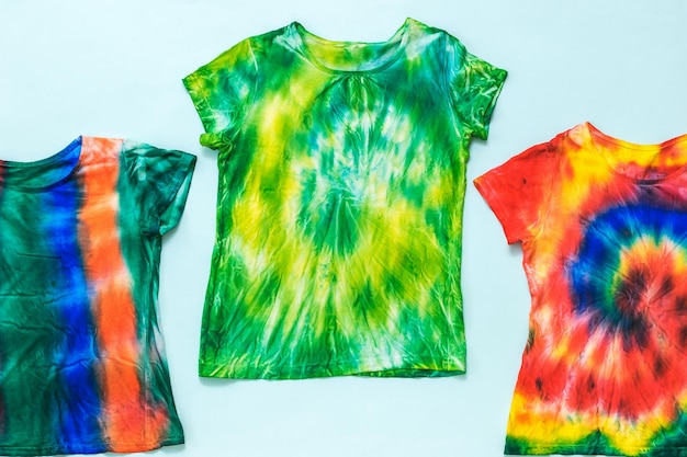 Photo set of tshirts decorated in tie dye style on a light background flat lay