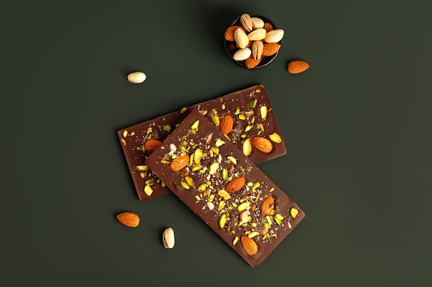 Set of two handmade chocolate bars with pistachios and almond on green background Sweet dessert