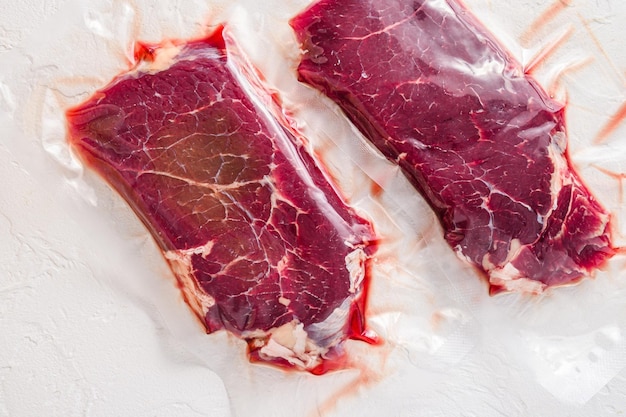 Set of vacuum packed organic beef meat rump steak on white concrete textured background side view selective focus