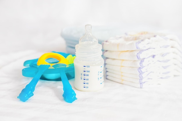 Set van baby plastic gerechten melk fles voeding knabbel blauw bestek lepel vork luiers speelgoed wegwerp luiers op de witte bed achtergrond