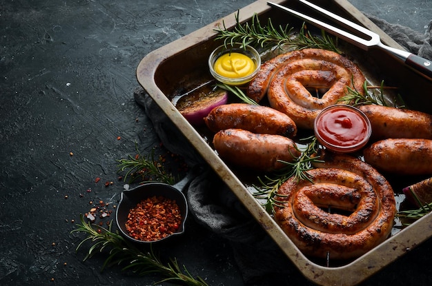 Set van gebakken barbecue worstjes met rozemarijn en sauzen. Bovenaanzicht. Op een zwarte stenen achtergrond.