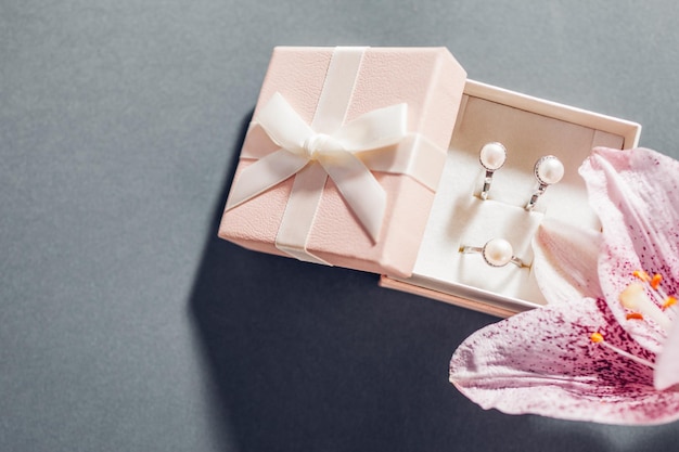 Set van pareljuwelen in roze geschenkdoos met bloemen Zilveren oorbellen en ring met lelie op grijze achtergrond