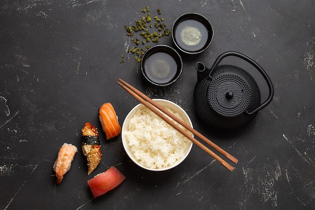 Set van traditioneel Japans eten: gekookte witte rijst, sushi, visrolletjes, groene thee in theepot op zwarte stenen achtergrond. Gerechten uit de Japanse keuken, van bovenaf, diner of lunch in Aziatische stijl