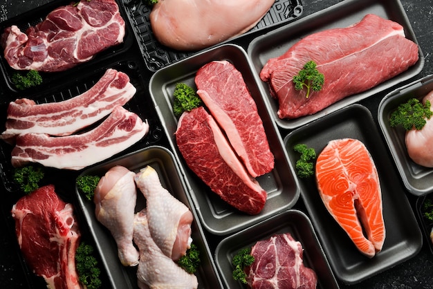 Set van vers rauw vlees en vis in plastic dozen kalfsvlees zalm steak kip varkensvlees Banner voor de supermarkt Op een donkere achtergrond Biologisch voedsel