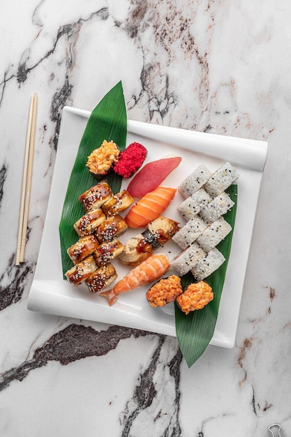 Set van verschillende kleurrijke maki sushi rolt nigiri en gunkan met tijgergarnalen tomago zalm tonijn chuka salade vliegende vis kaviaar tonijn en groen bamboeblad in een bovenaanzicht van een witte keramische plaat