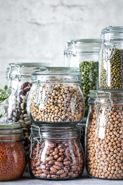 Set van verschillende peulvruchten in glazen potten op, betonnen witte tafel. Een eiwitbron voor vegetariërs. Het concept van gezond eten en voedselopslag.