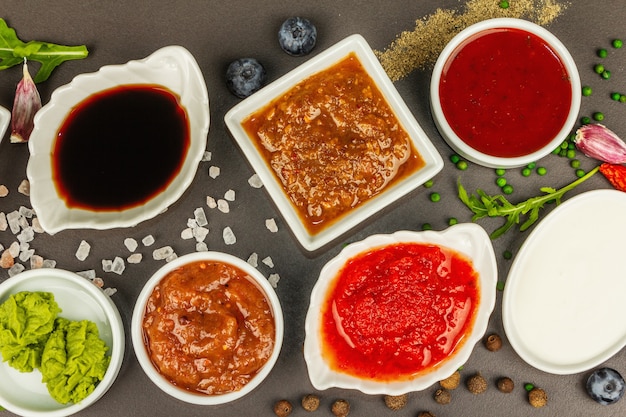 Set van verschillende sauzen - ketchup, mayonaise, barbecue, soja, chutney, wasabi, adjika, mierikswortel, aioli, marinara. Donkere stenen betonnen achtergrond, bovenaanzicht