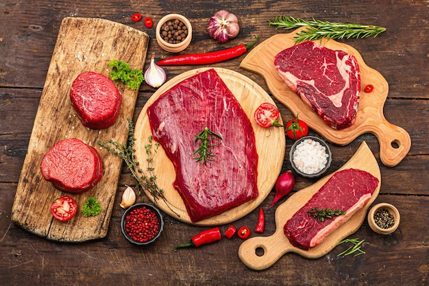 Set van verschillende steaks met traditionele specerijen en kruiden Vers rauw vlees omvat ribeye ronde flank en lendenbiefstuk Oude houten achtergrond plat bovenaanzicht