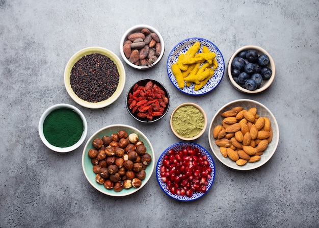 Set van verschillende superfoods in kommen op steengrijze achtergrond: spirulina, gojibes, cacao, matcha groene theepoeder, quinoa, chiazaden, bosbessen, noten voor gelukkig gezond leven, bovenaanzicht, close-up