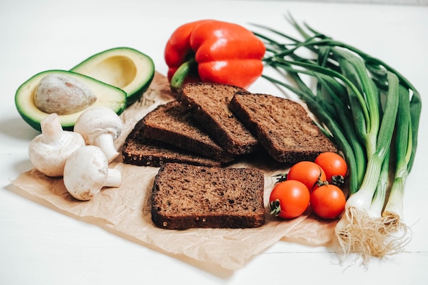 Set van verschillende verse groenten met sneetjes bruin brood op een witte houten tafel achtergrond. Kopiëren, lege ruimte voor tekst