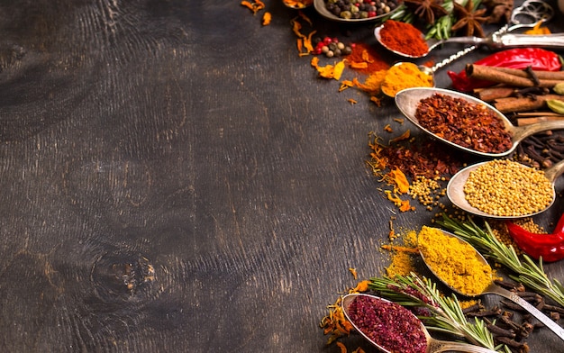 Set of various aromatic colorful spices in old vintage spoons and herbs on a dark wooden background.