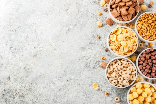 Insieme di vari cereali per la colazione, fiocchi di mais, sbuffi, pop, tavolo in pietra grigia copia spazio vista dall'alto