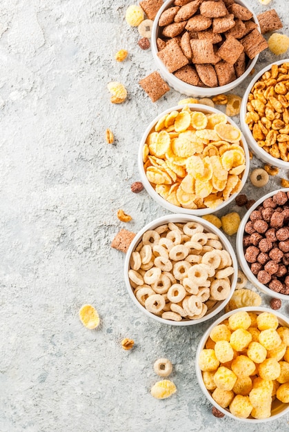 Set of various breakfast cereal corn flakes, puffs, pops, grey stone table copy space top view