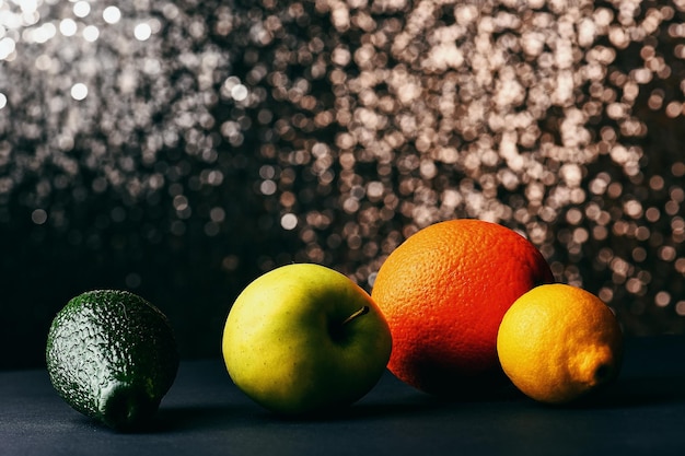 Набор различных фруктов лимон, яблоко, апельсин, авокадо на сером столе, студия, сверкающий фон, вид сбоку