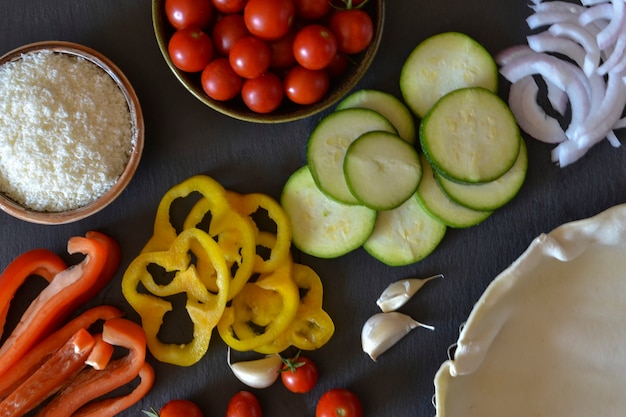 Foto set di verdure (peperone, cipolla, zucchine, pomodori) e parmigiano su sfondo nero. ingredienti per la torta di insalata. vista dall'alto.