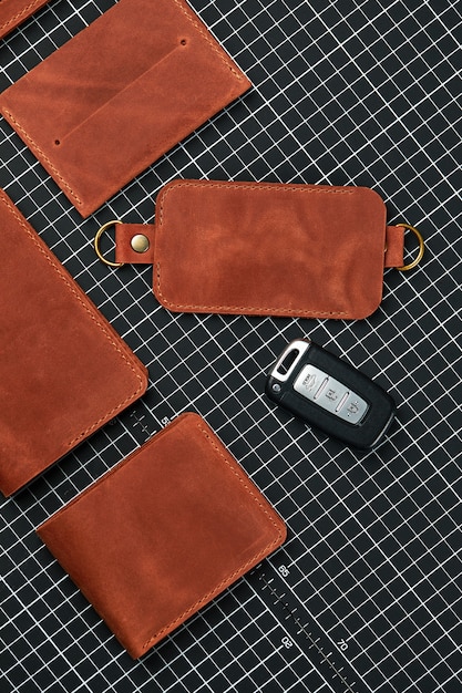 A set of wallets, business card holders and key holders made of handmade leather, made of red leather on a table for cutting leather, surrounded by tools, demonstration of handmade leather products.