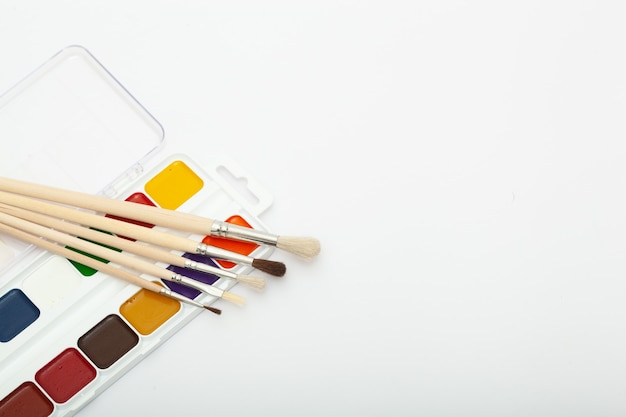 A set of watercolor paints and paint brushes on a white background with a copy space for text. Close-up