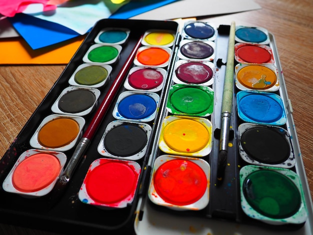 A set of watercolors of different colors for drawing Multicolored round containers with bright paint Tools for the lesson of drawing and labor Colored paper Red blue yellow green colors