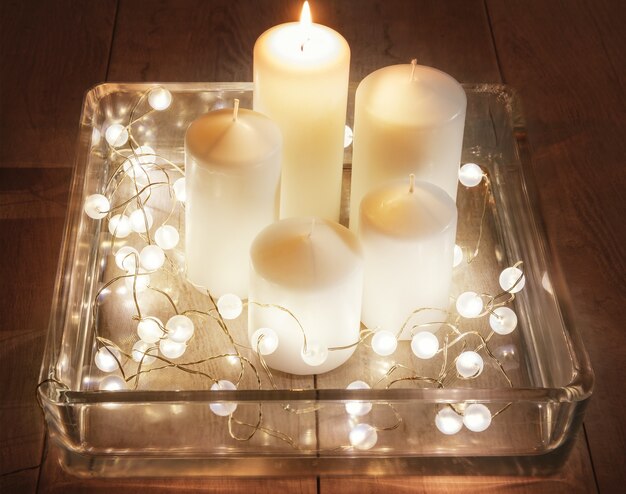 Set of white candles and garland in a large glass candlestick on a wooden background. The concept of Christmas, Advent, winter holidays.