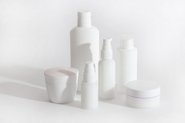 Foto set di flaconi cosmetici bianchi e vasetti con ombre dure. concetto di cura della casa e del salone di bellezza
