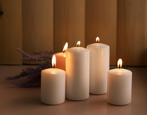 Set of white and pink burning wax candles with lavender on the\
wood background in low lights